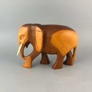 May include: A wooden elephant figurine with a carved ivory tusk. The elephant is brown and has a detailed, stylized design.