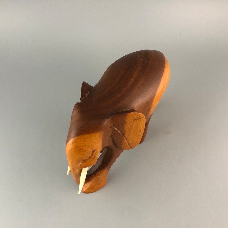 May include: A wooden elephant figurine with a brown finish and carved details. The elephant has ivory tusks and is positioned in a walking pose.