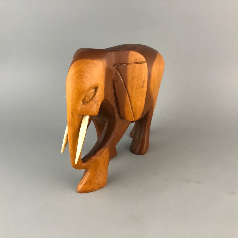May include: A wooden elephant sculpture with carved details and ivory-colored tusks. The elephant is standing with its head lowered and its trunk curled.