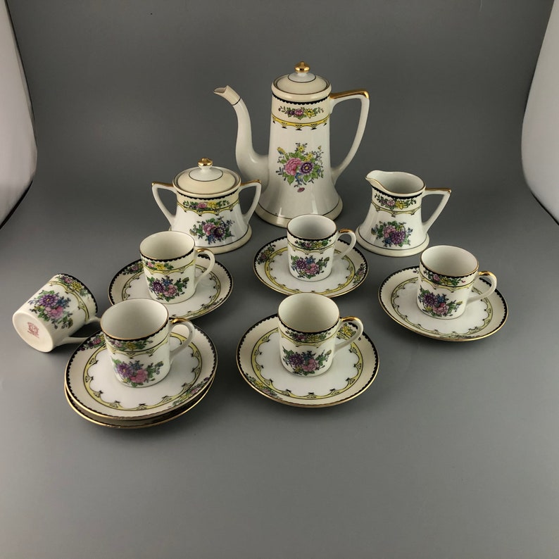 May include: A vintage porcelain tea set with floral designs in shades of pink, purple, and yellow. The set includes a teapot, creamer, sugar bowl, and six cups and saucers.