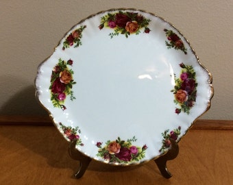 May include: A white oval serving plate with a gold rim and a floral design featuring red, pink, and yellow roses. The plate has two handles on the sides.