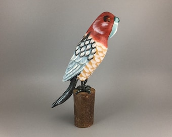 May include: Hand-painted wooden bird figurine with blue, red, and yellow colors. The bird is perched on a wooden stand.