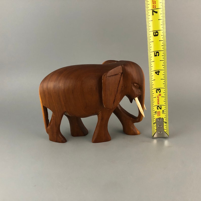 May include: A hand-carved wooden elephant figurine with ivory tusks. The elephant is brown and has a detailed, realistic design. It is approximately 4 inches tall.