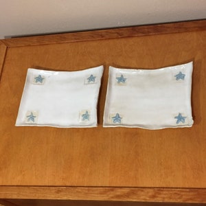 May include: Two white ceramic rectangular plates with blue star designs. The plates have a slightly wavy edge.