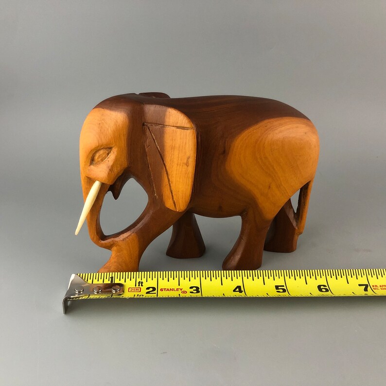 May include: A wooden elephant figurine with a carved ivory tusk. The elephant is standing on all four legs and has a brown wood finish.