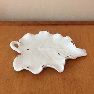 May include: White ceramic leaf-shaped serving tray with a handle. The tray has a distressed finish, giving it a vintage look.