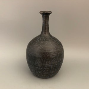Może przedstawiać: Brązowy ceramiczny wazon o okrągłym korpusie i wąskiej szyjce. Wazon jest ozdobiony białym, wirującym wzorem.