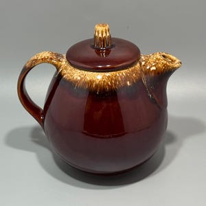 Peut inclure: Une théière ronde en céramique avec une glaçure marron brillant profond et une glaçure contrastante beige et beige clair de style goutte autour du bord, du couvercle, de l'anse et du bec. Elle comprend un couvercle assorti avec un bouton texturé.