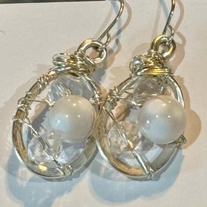 May include: Silver wire wrapped earrings with a clear crystal and a white pearl in each earring.