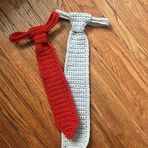 May include: Two crocheted ties, one red and one grey, lying on a wooden surface.