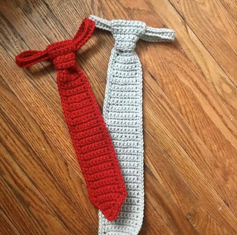 May include: Two crocheted ties, one red and one grey, lying on a wooden surface.