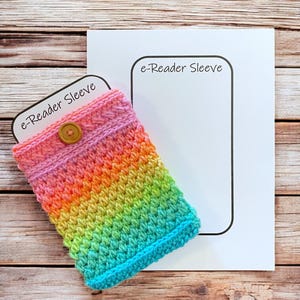 May include: A rainbow-colored crochet e-reader sleeve with a button closure. The sleeve transitions from pink to orange, yellow, green, and blue. The words "e-Reader Sleeve" are printed on a white card.