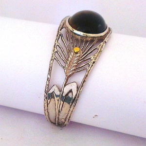 Könnte beinhalten: Silberarmband mit einem dunkelbraunen Edelstein und einem goldenen Akzent. Das Armband ist mit einem filigranen, komplizierten Muster verziert.