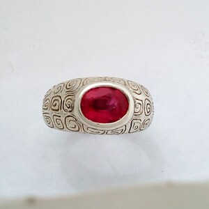 May include: A silver ring with a red gemstone set in a swirl pattern.