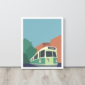 May include: A green and white Boston T train with the word "BOSTON" on the front, driving through a city street with a brick building and trees in the background.