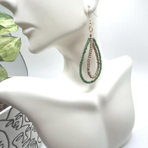 May include: A pair of dangle earrings with a teardrop shape. The earrings are made with green and gold beads.