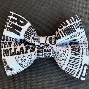May include: A black and white bow tie with a newspaper print design. The fabric features various text fragments and graphic elements, creating a vintage aesthetic. The bow tie is a stylish accessory for formal or themed events.