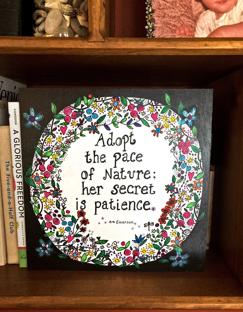 May include: A black canvas print featuring a colourful floral wreath surrounding the text "Adopt the pace of Nature; her secret is patience." The quote is attributed to Emerson.