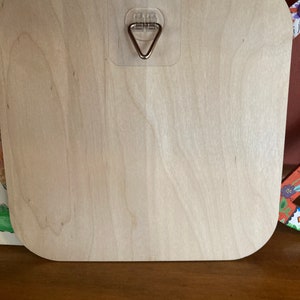 May include: A light wood square sign with rounded corners. The sign has a clear plastic hook attached to the back.