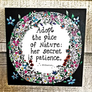 May include: Black and white art print with a floral wreath surrounding a quote that reads "Adopt the pace of nature; her secret is patience." The quote is attributed to Emerson.
