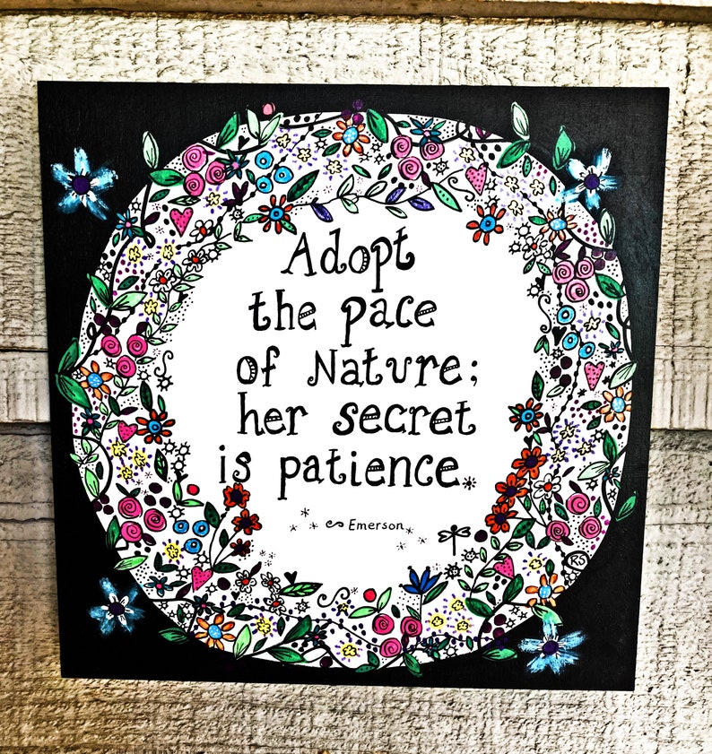 May include: Black and white art print with a floral wreath surrounding a quote that reads "Adopt the pace of nature; her secret is patience." The quote is attributed to Emerson.
