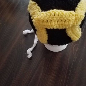 May include: A black and white crocheted hat with a yellow crocheted band. The hat has a white pom pom on top.