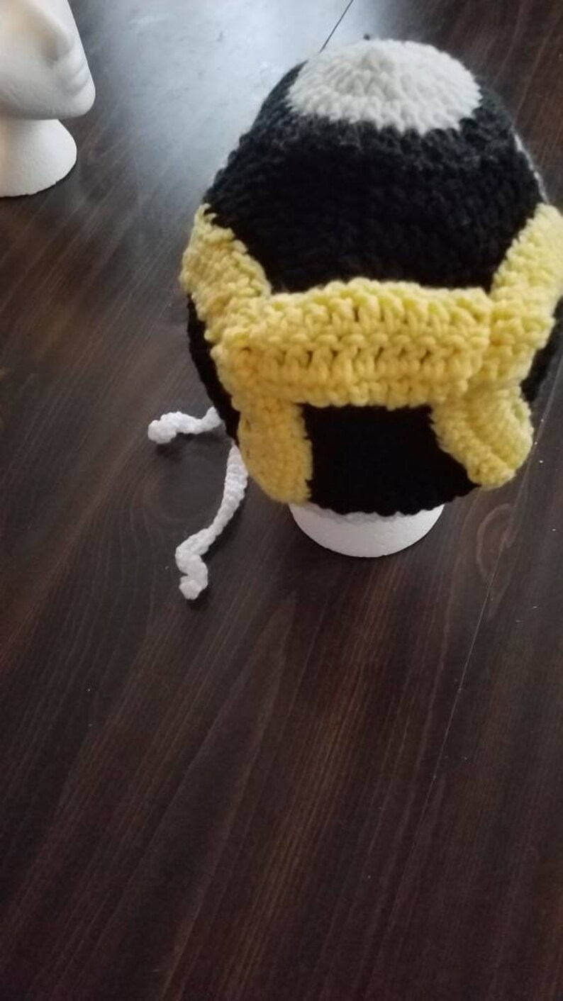 May include: A black and white crocheted hat with a yellow crocheted band. The hat has a white pom pom on top.