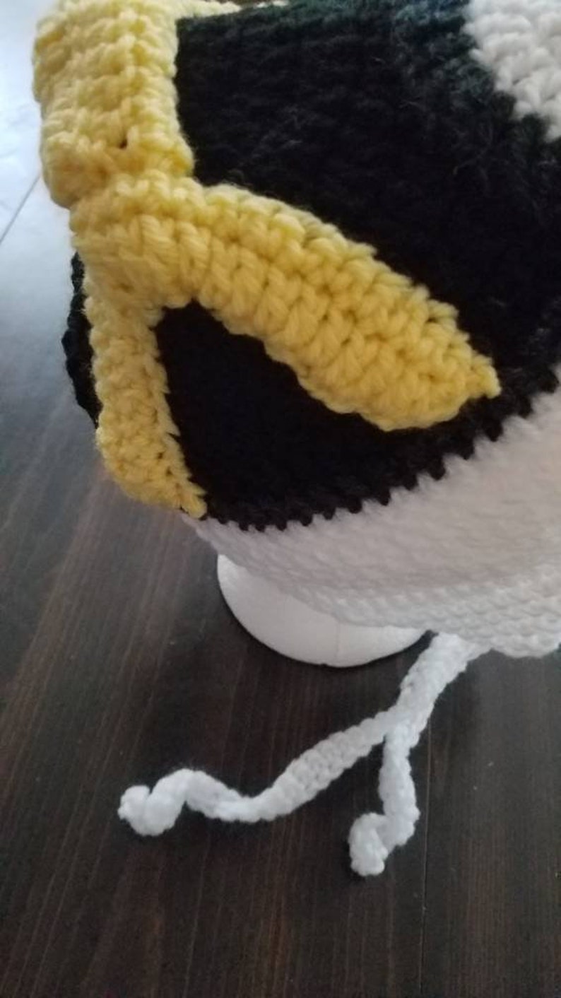 May include: A crocheted hat with black, white, and yellow stripes. The hat has a white crocheted tie.