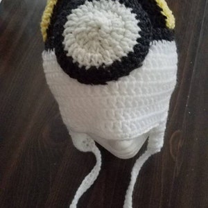 May include: White crocheted hat with a black and white circle design and a yellow brim. The hat has white ties.