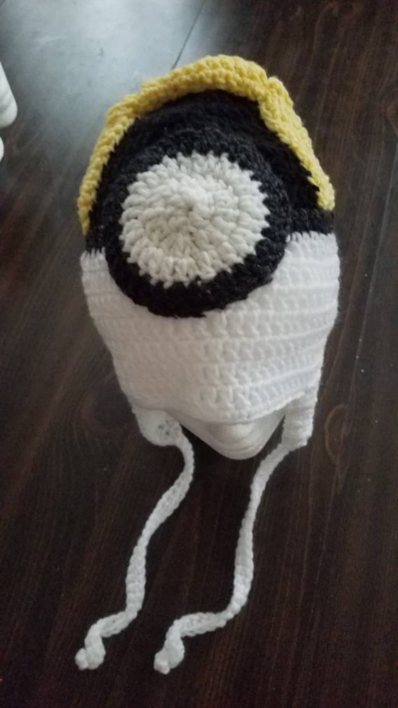 May include: White crocheted hat with a black and white circle design and a yellow brim. The hat has white ties.