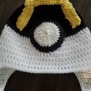 May include: White crocheted hat with a black and white pokeball design and yellow crocheted accents.