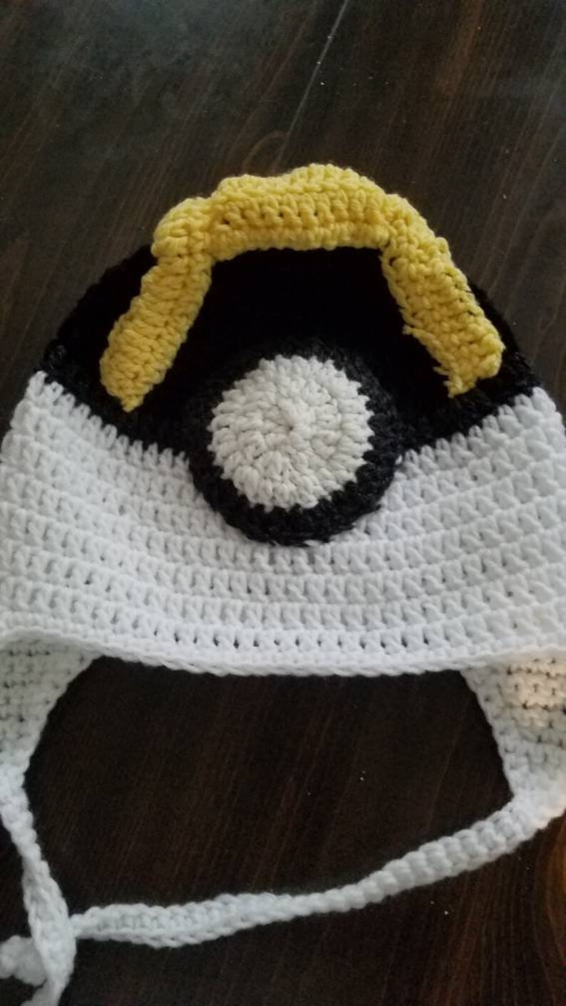 May include: White crocheted hat with a black and white pokeball design and yellow crocheted accents.
