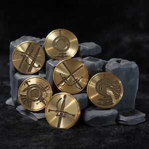 以下が含まれることがあります： 異なるデザインの金色の金属製のメダルが6つ。各メダルには、剣、船、その他の抽象的なパターンなど、ユニークなデザインが施されています。