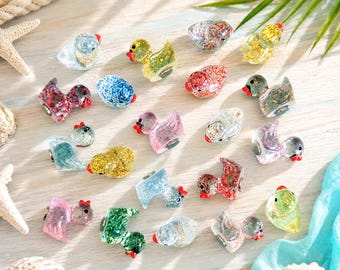 May include: A collection of small, duck-shaped figurines made of translucent resin filled with various colored glitter. Each duck features a distinct color, including gold, blue, pink, green, and silver, with a small red beak and black eyes.