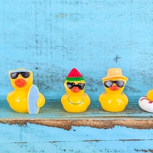 May include: Five yellow rubber ducks arranged in a row. The first wears a blue hat and sunglasses, the second has sunglasses and a surfboard, the third wears a watermelon hat and sunglasses, the fourth has a tan hat and sunglasses, and the fifth wears heart-shaped sunglasses and sits in a white and red life ring.