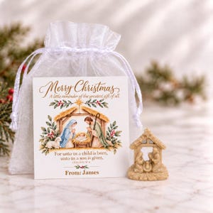 May include: A white sheer organza drawstring bag containing a card with a nativity scene illustration and the text Merry Christmas, A little reminder of the greatest gift of all, For unto us a child is born, unto us a son is given, Isaiah 9:6, From: James, and a small beige nativity figurine.