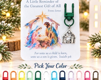 May include: A white display card featuring a watercolor nativity scene, the text A Little Reminder of the Greatest Gift of All, From: James, and Isaiah 9:6. A silver-toned metal nativity charm is attached to a dark green swivel lobster clasp.