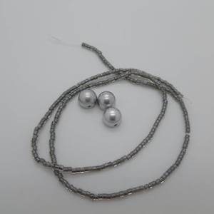 May include: A silver beaded necklace with three silver beads. The beads are round and have a smooth surface.