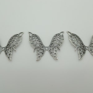May include: Three silver metal butterfly charms with intricate cut-out designs. The charms are delicate and have a vintage look.