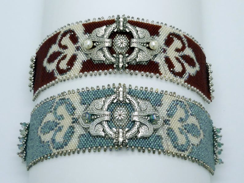 K&ouml;nnte beinhalten: Zwei Perlenarmb&auml;nder mit silberfarbenen Verschl&uuml;ssen. Das obere Armband hat ein braunes und wei&szlig;es Muster mit einem Perlenakzent. Das untere Armband hat ein blaues und wei&szlig;es Muster mit einem klaren Kristallakzent.