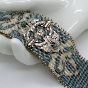 K&ouml;nnte beinhalten: Ein blaues und wei&szlig;es Perlenarmband mit einem verzierten silbernen Verschluss. Das Armband ist aus kleinen Perlen gefertigt und hat ein geometrisches Muster.
