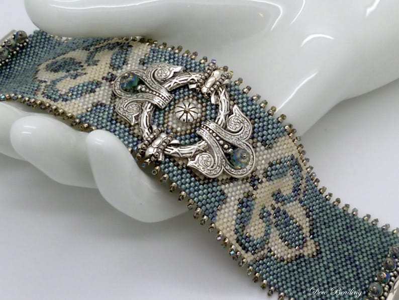 K&ouml;nnte beinhalten: Ein blaues und wei&szlig;es Perlenarmband mit einem verzierten silbernen Verschluss. Das Armband ist aus kleinen Perlen gefertigt und hat ein geometrisches Muster.
