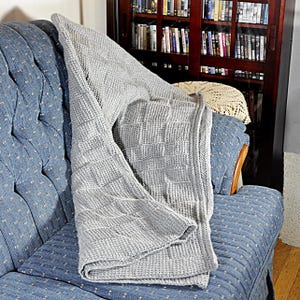 May include: A gray knitted throw blanket with a waffle stitch pattern is draped over a blue couch.