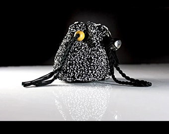 May include: A small, crocheted drawstring pouch in black and white. The pouch has a repeating pattern and is accented with a wooden bead and a silver charm. The black drawstring has tassels at the ends.
