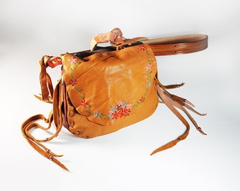May include: A brown leather satchel bag with a floral embroidery design. The bag has a long strap and fringe details.