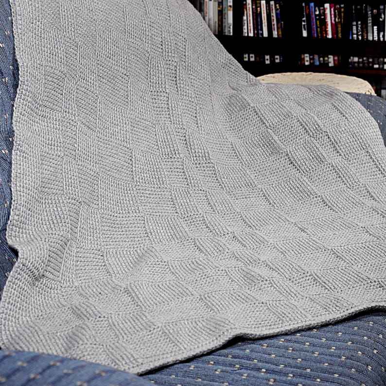 May include: A gray knitted throw blanket with a woven pattern. The blanket is draped over a chair.