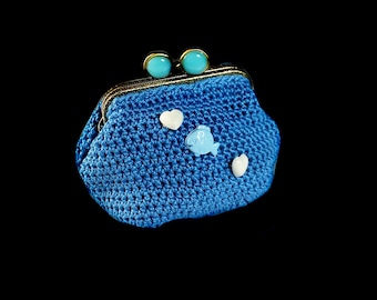 May include: A small blue crocheted coin purse with a gold clasp and blue and white plastic embellishments in the shape of hearts and a fish.