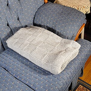 May include: A gray knitted throw blanket with a textured pattern is placed on a blue patterned armchair.