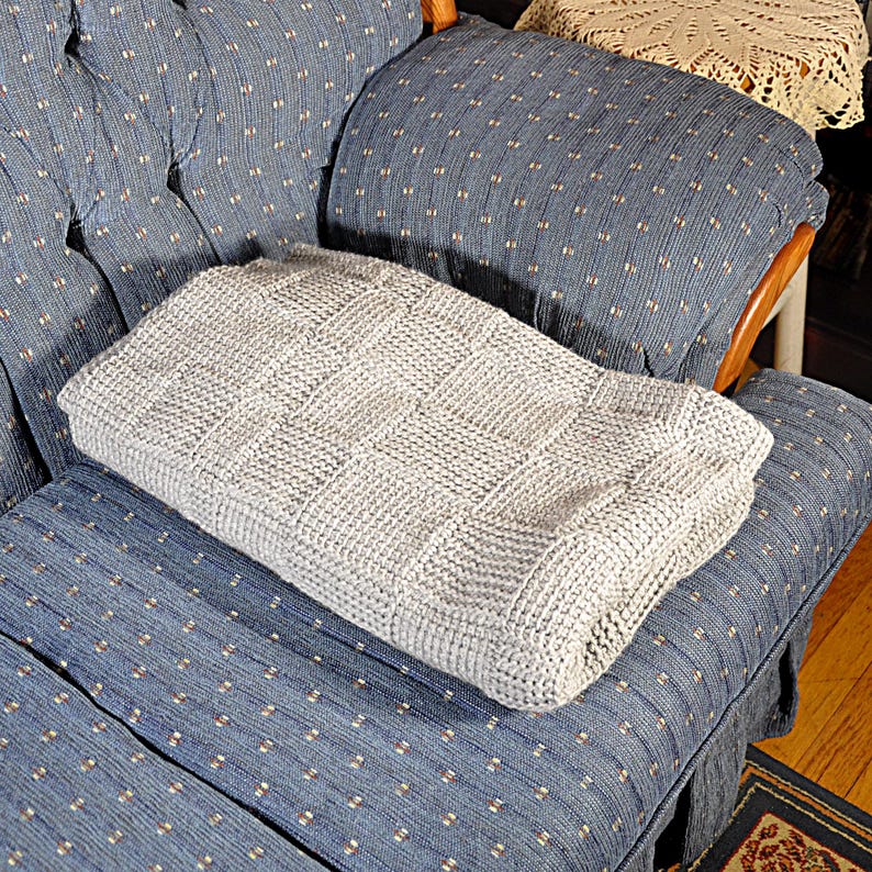 May include: A gray knitted throw blanket with a textured pattern is placed on a blue patterned armchair.