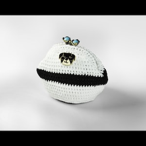 May include: White crocheted coin purse with a black stripe and a gold dog pin. The purse is shaped like a football.